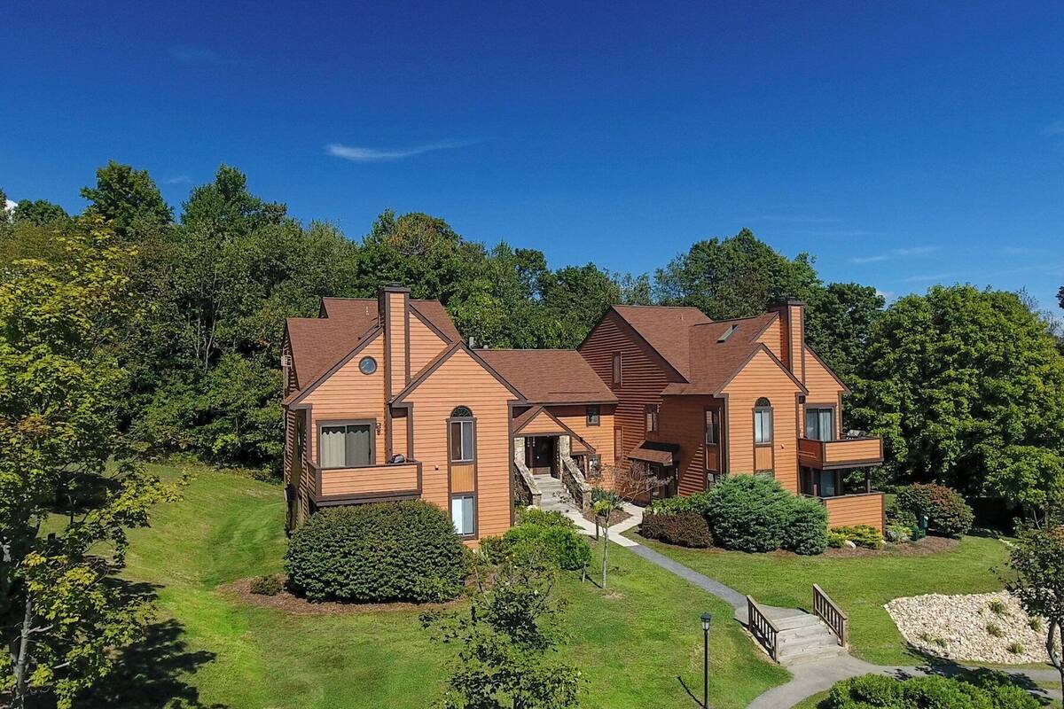 A large, multi-story wooden house with a central staircase and a well-maintained lawn.