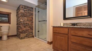 A bathroom with a stone accent wall, a glass shower enclosure, a toilet, wooden cabinets, and a mirror.
