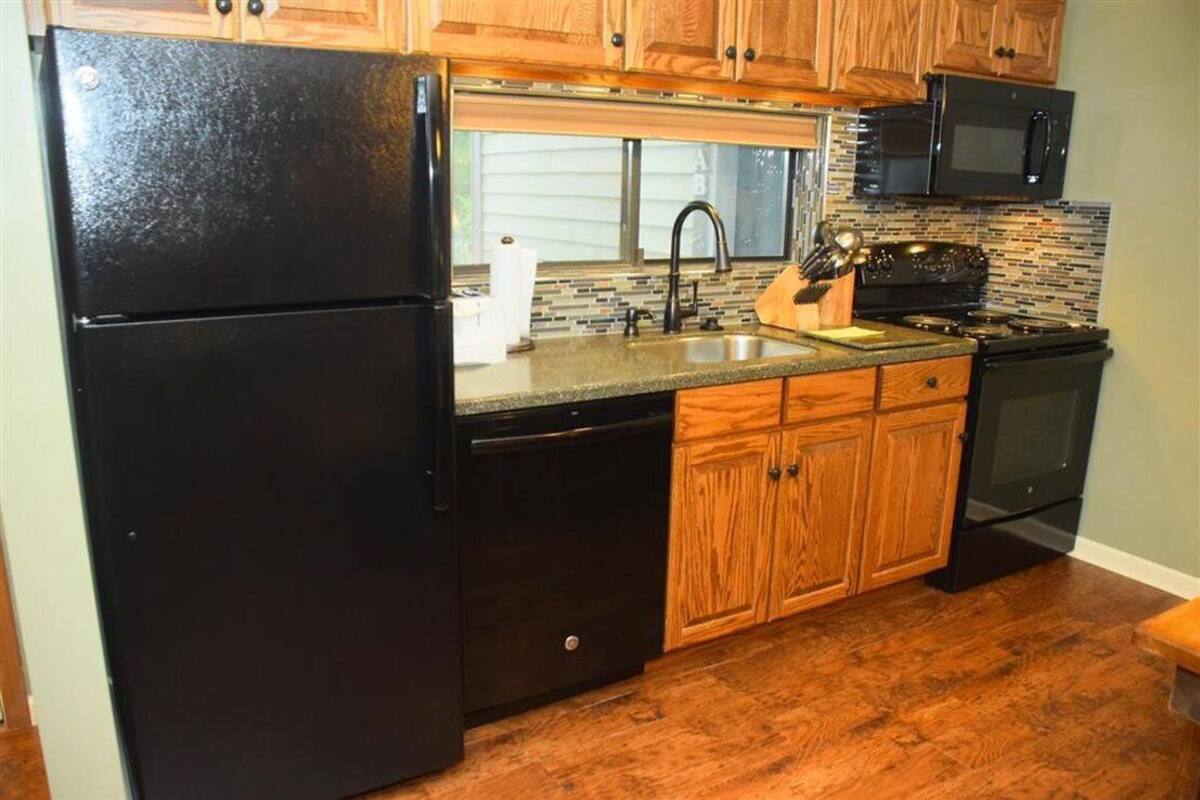 A kitchen with wooden cabinets, a black refrigerator, a microwave, and a stove.