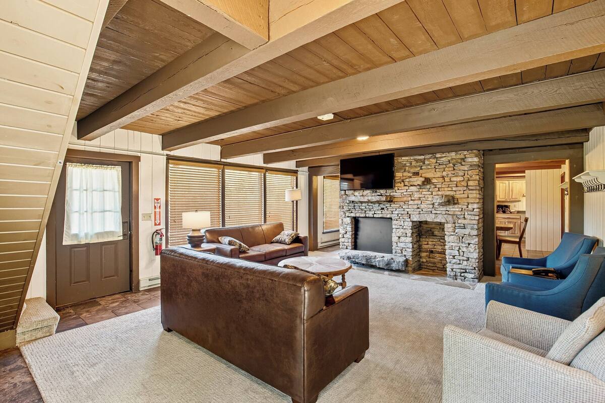 A spacious living room with a stone fireplace, a brown leather sofa, and a blue armchair.