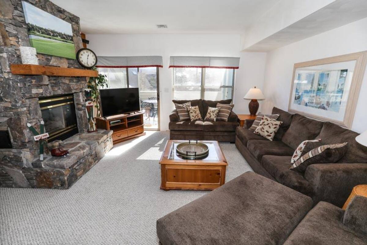 A cozy living room with a stone fireplace, a flat-screen TV, a brown sofa, and a coffee table.