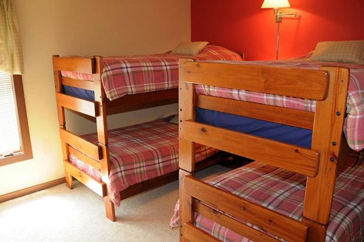 A room with three bunk beds, a red wall, and a lamp.