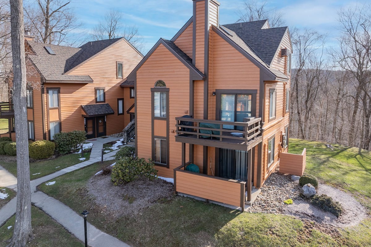A modern two-story house with a balcony, a covered porch, and a small front yard with a pathway.