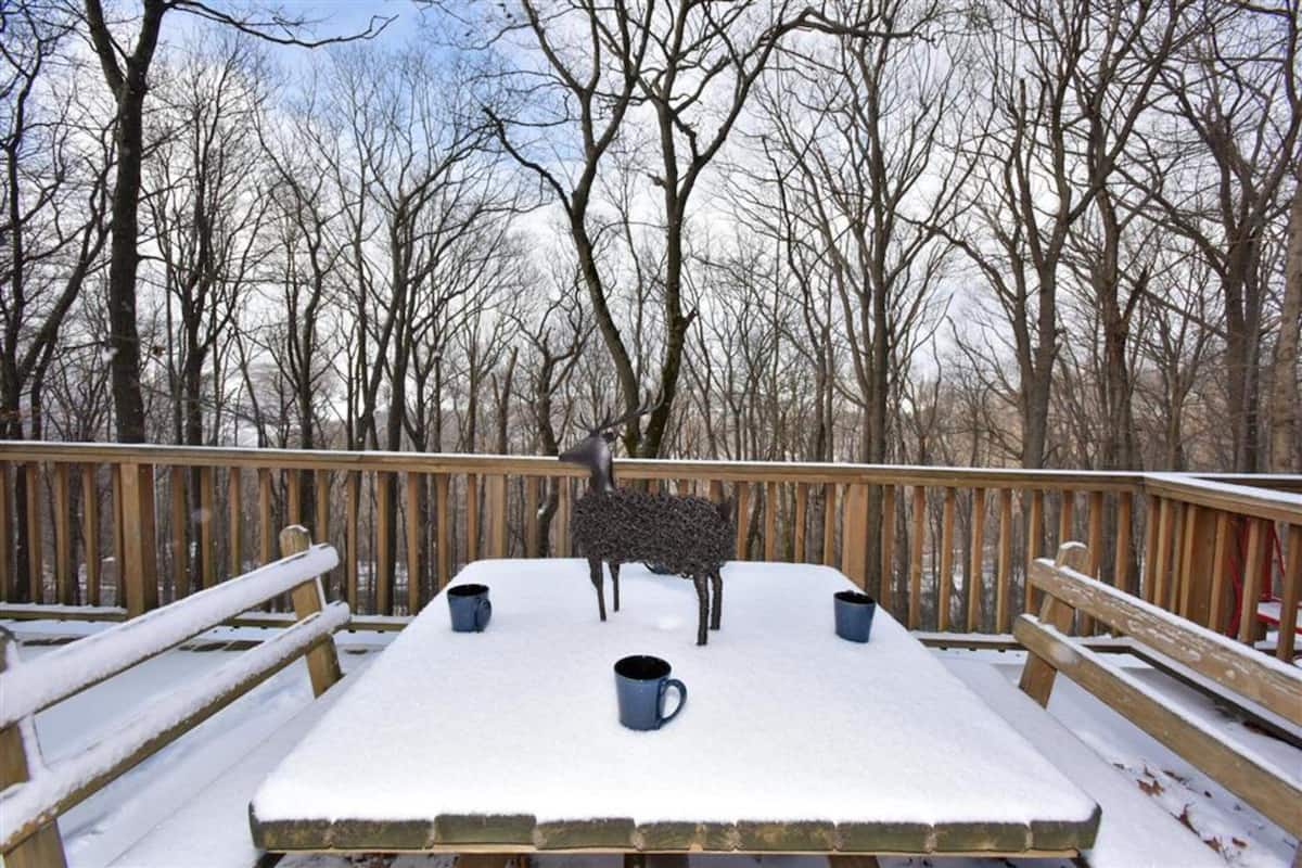 A snow-covered deck with a wooden railing, a table, and four cups.
