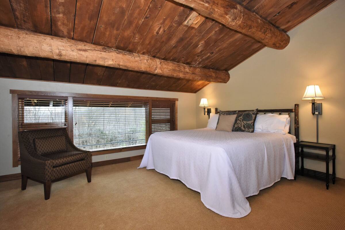 A bedroom with a large bed, a chair, and two wall-mounted lamps.