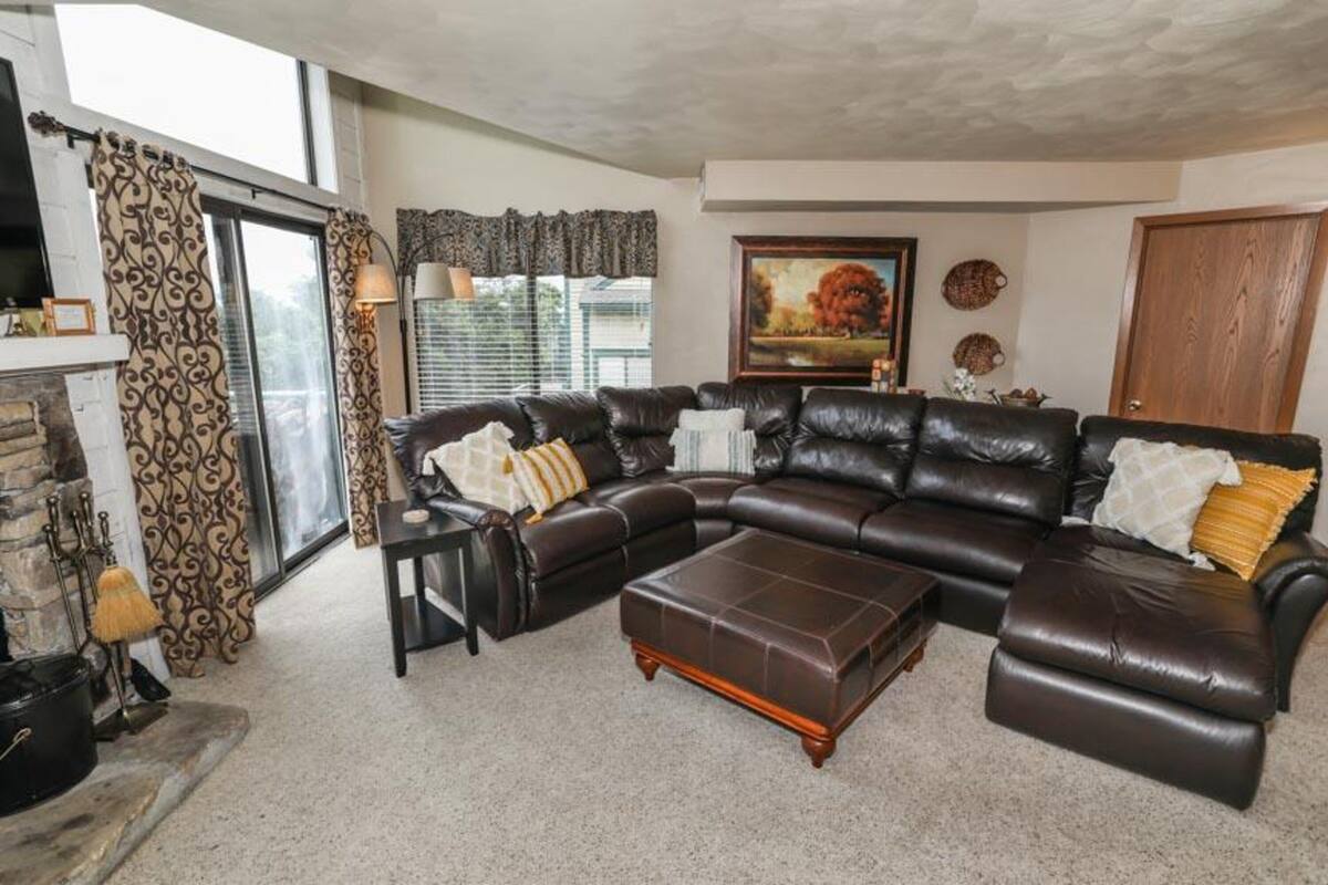 A living room with a large L-shaped leather sofa, a wooden coffee table, and a fireplace with a stone mantle.