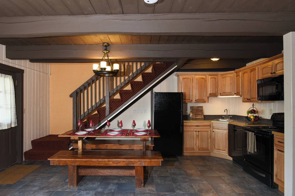 A kitchen with wooden cabinets, a black refrigerator, a stove, and a dining table set with red napkins and wine glasses.