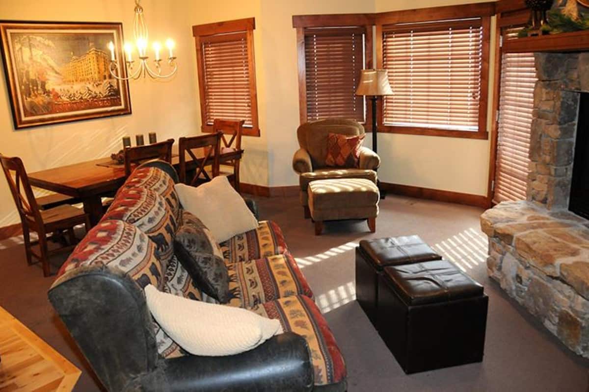A living room with a sofa, armchair, ottoman, dining table, chairs, and a fireplace.