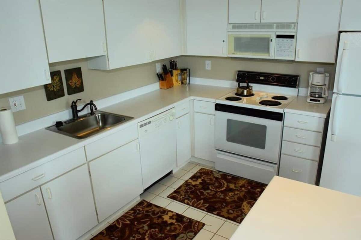 A compact kitchen with white cabinets, a microwave, a stove, and a coffee maker.