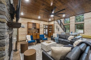 Ein gemütliches Blockhaus-Interieur mit Kamin, Essbereich und einer Treppe, die in einen oberen Bereich führt.