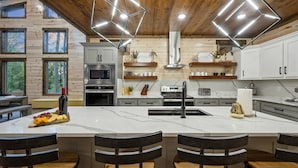Une cuisine moderne dotée d’un grand îlot central, de meubles blancs et d’un plafond en bois.