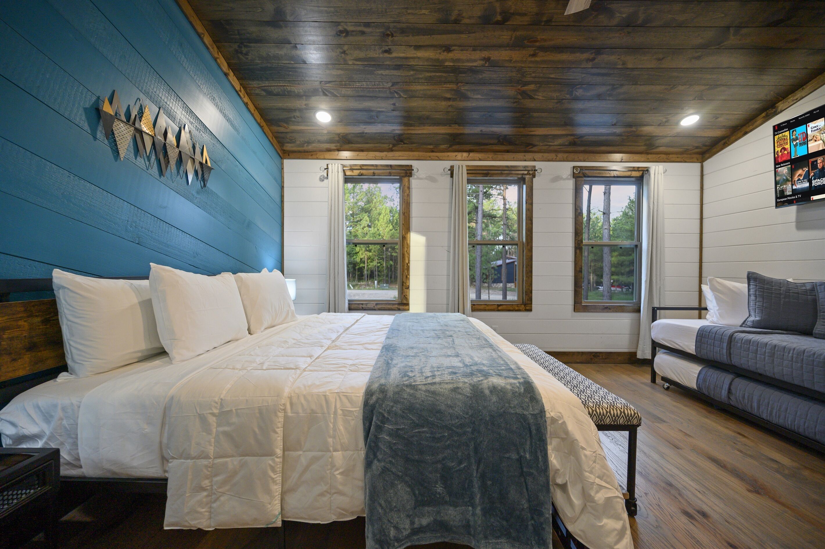 A bedroom with a large bed, a bench, a sofa, and a TV on the wall.