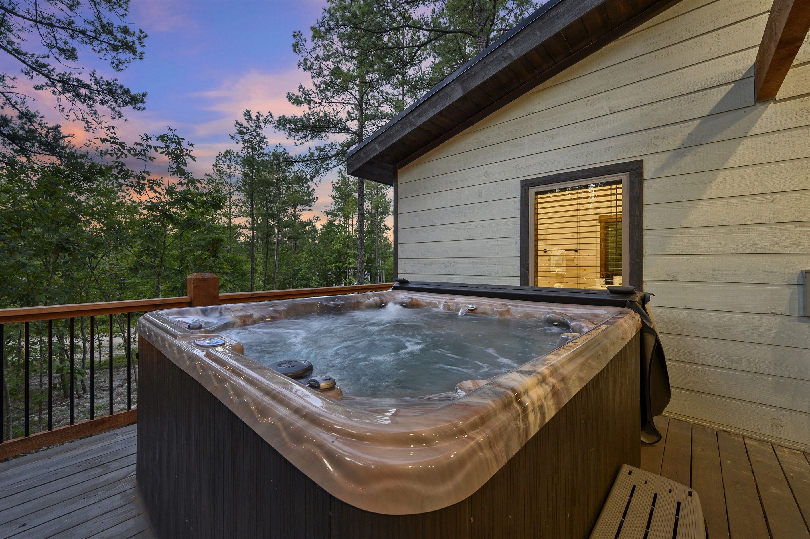 A hot tub on a wooden deck with a view of trees and a sunset.