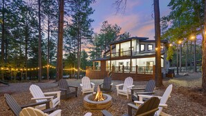 Un chalet doté d’un foyer et de chaises Adirondack, situé dans un cadre forestier.