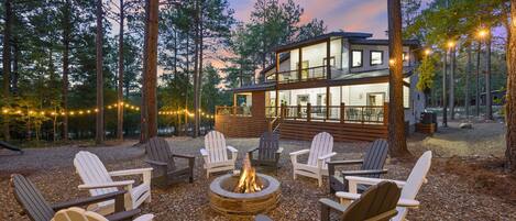 Eine Lodge mit Feuerstelle und Adirondack-Stühlen in einer Waldlandschaft.