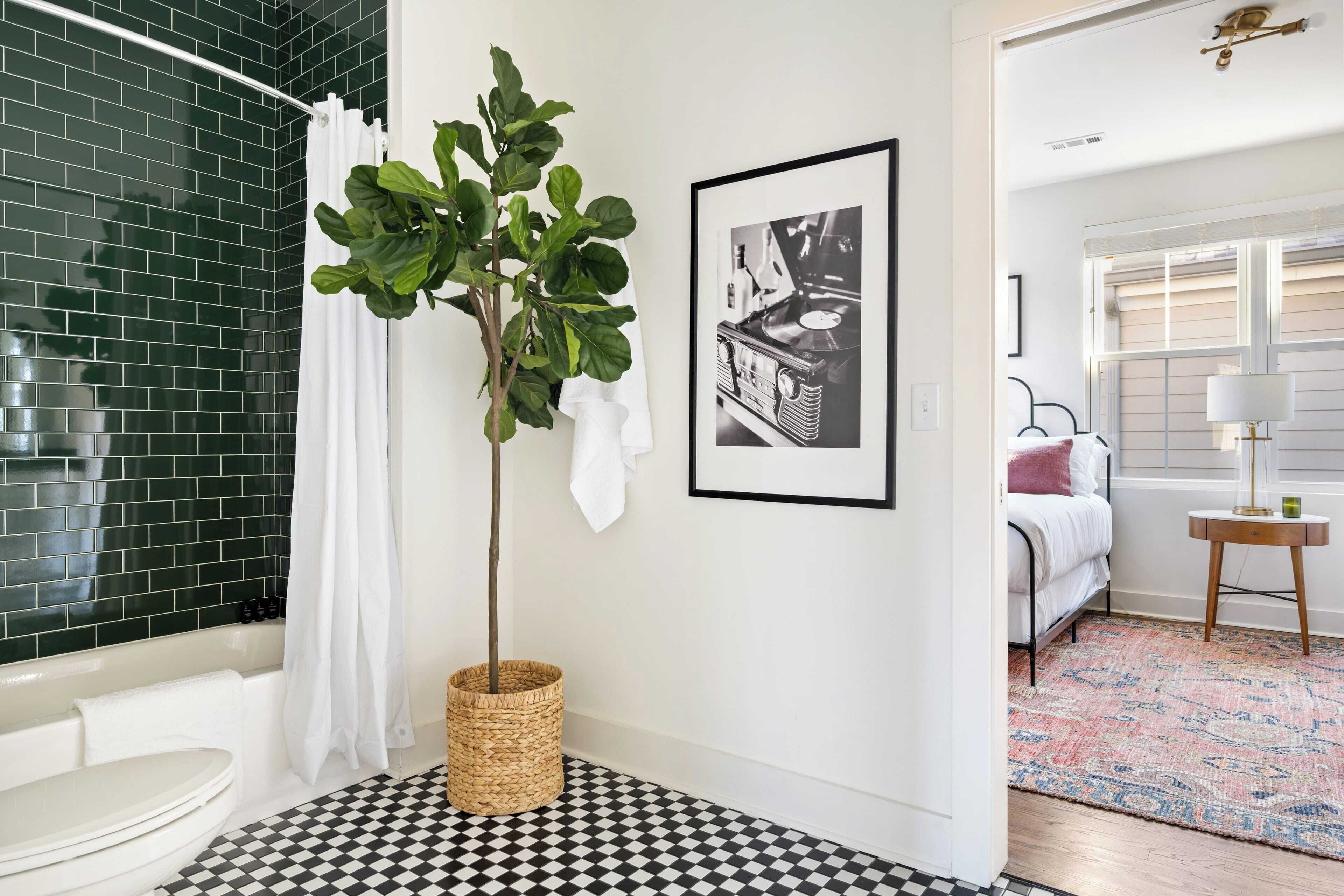Un baño con piso a cuadros, zona de ducha con azulejos verdes, lavamanos blanco y un cuadro en la pared.