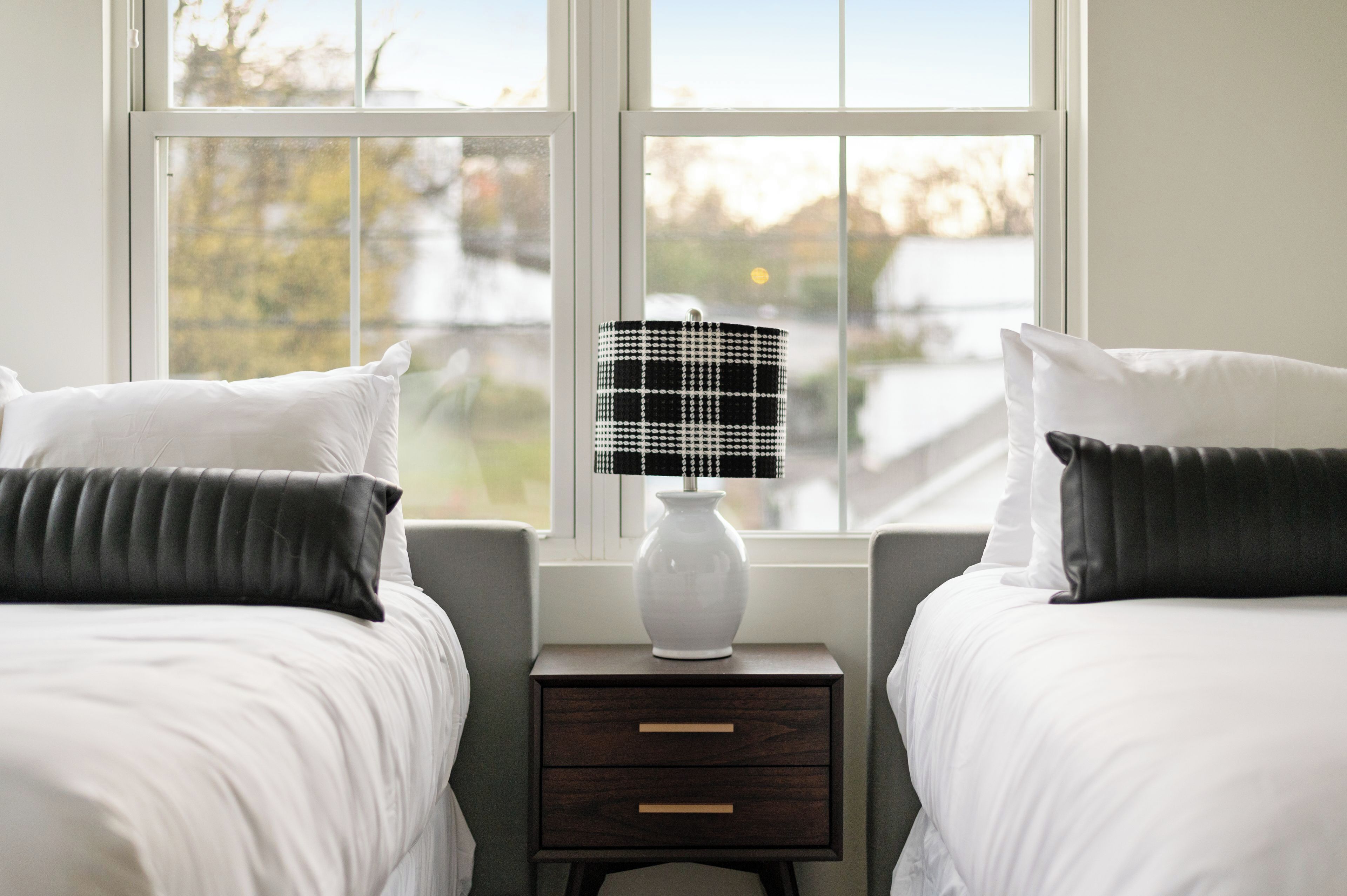 A bedroom with two beds, a nightstand with a lamp, and a window with a view.