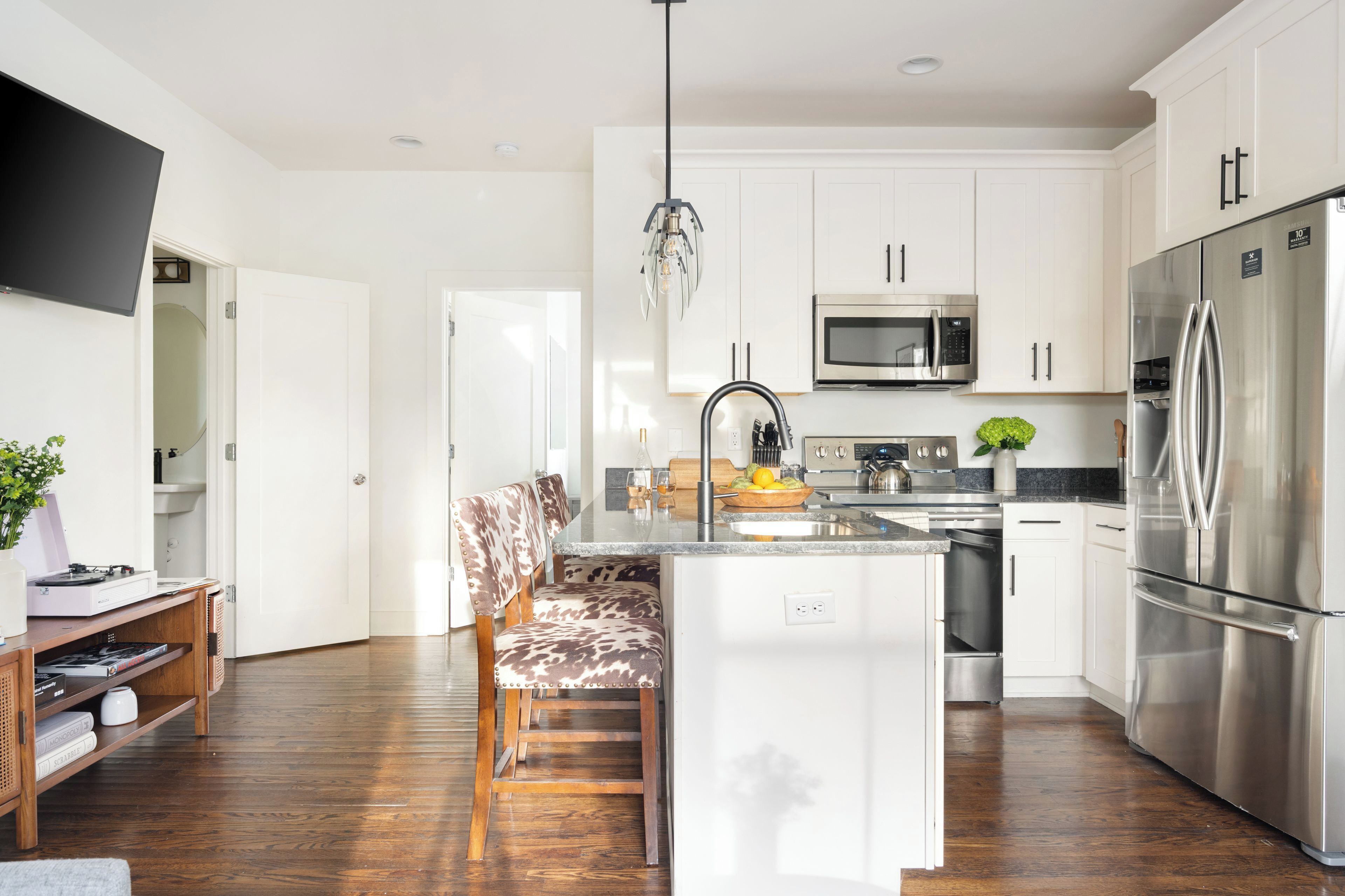A modern kitchen with white cabinets, stainless steel appliances, a central island, and a bar seating area.