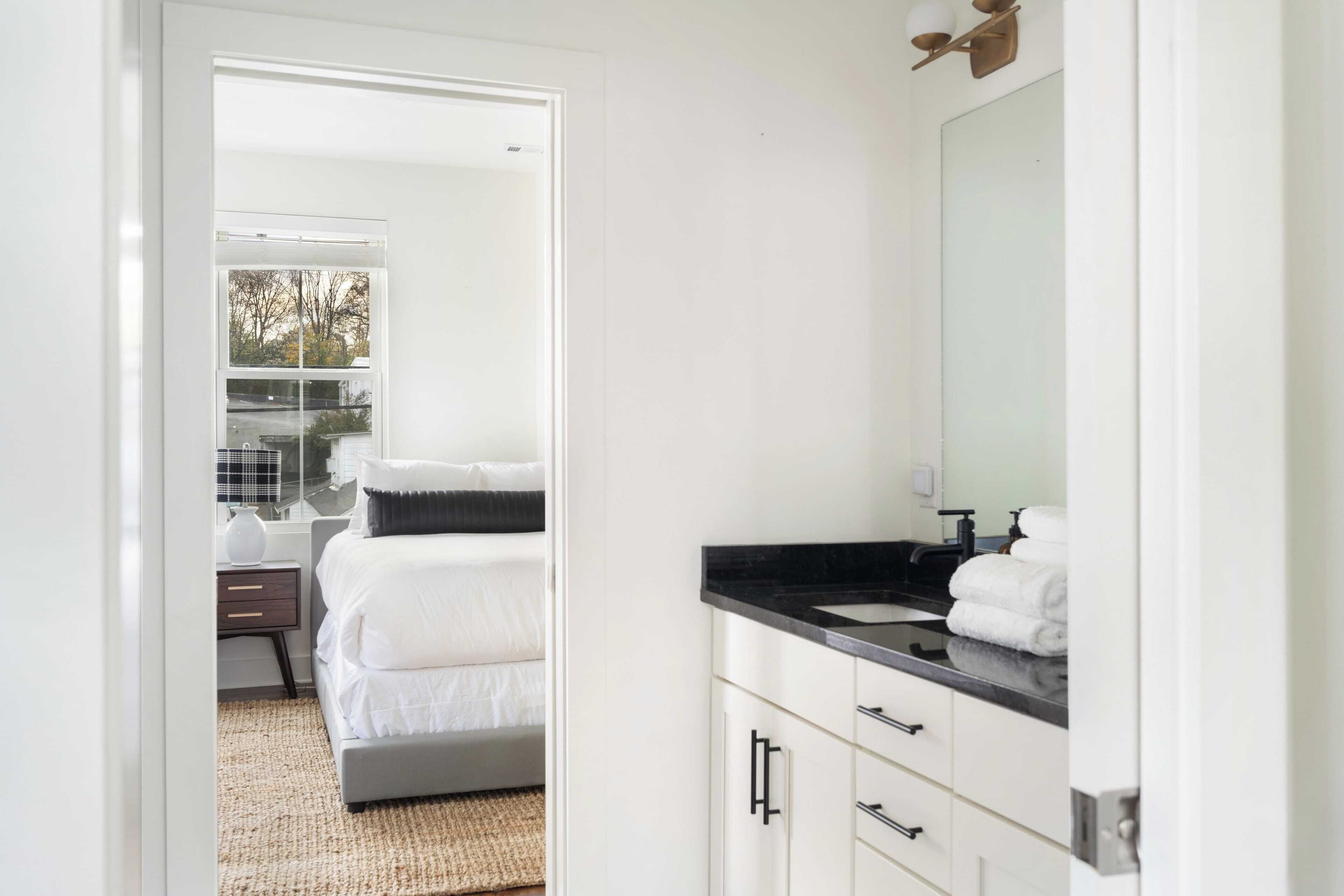 A modern hotel room with a bed, a bathroom with a black countertop, and a large mirror.