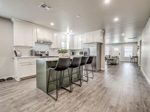 Una cocina amplia con armarios blancos, una isla central con taburetes y un área de comedor al fondo.
