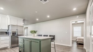 Una cocina moderna con una isla central, armarios blancos y electrodomésticos de acero inoxidable.