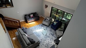 A modern living room with a grey sofa, a grey armchair, a coffee table, and a large window with a view of greenery. - Huntington Northport Spacious Gorgeous Getaway for family reunion or business (Northport)