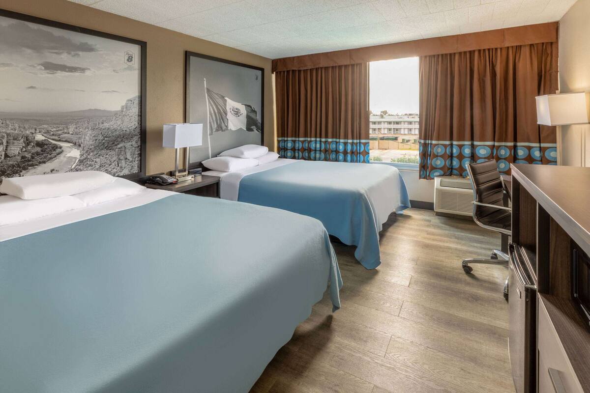 A hotel room with two beds, a desk, a chair, and a large window with curtains.