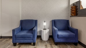 Two blue armchairs facing each other with a white side table between them, a herringbone-patterned wall, and a modern mirror with geometric decor. - Super 8 by Wyndham Laredo (Laredo)