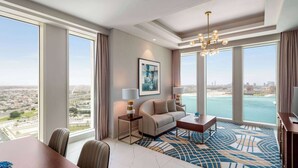 Une chambre d’hôtel spacieuse dotée d’une grande fenêtre donnant sur la ville, d’un lustre moderne, d’un canapé et d’un coin repas.
