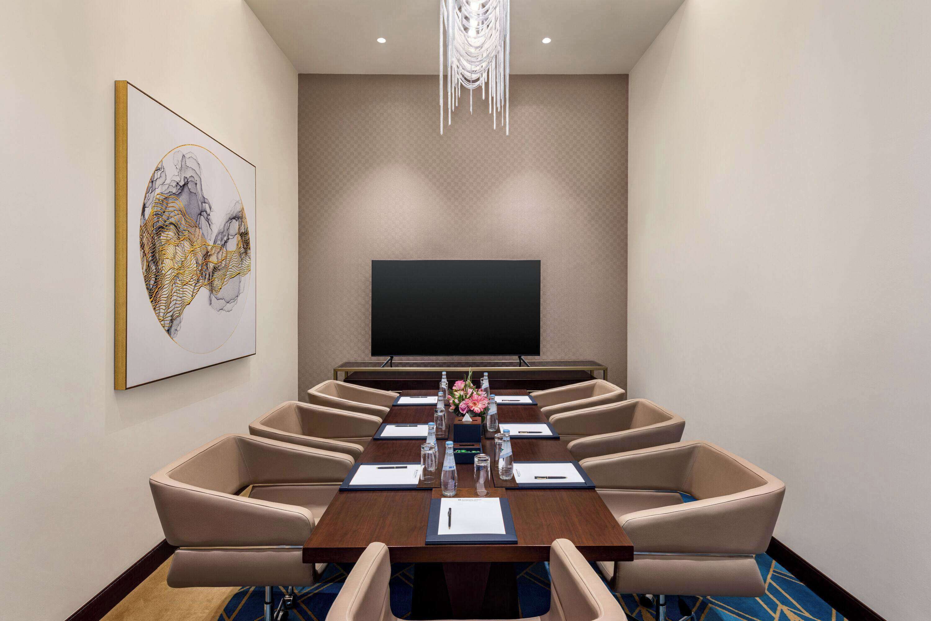 Un salón de conferencias con una gran mesa, sillas, un televisor de pantalla plana y un cuadro decorativo en la pared.