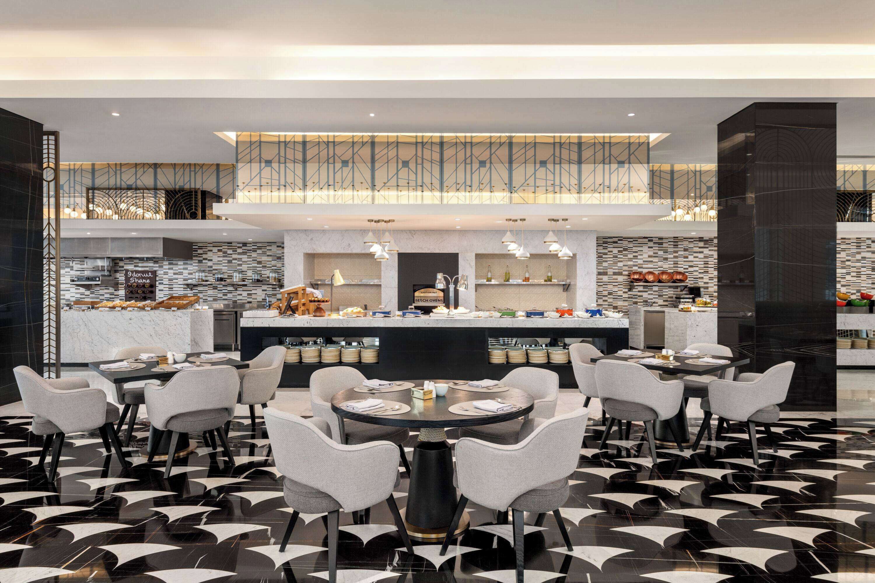 Un restaurante moderno con un área de comedor central, una cocina al fondo y un suelo con diseño.