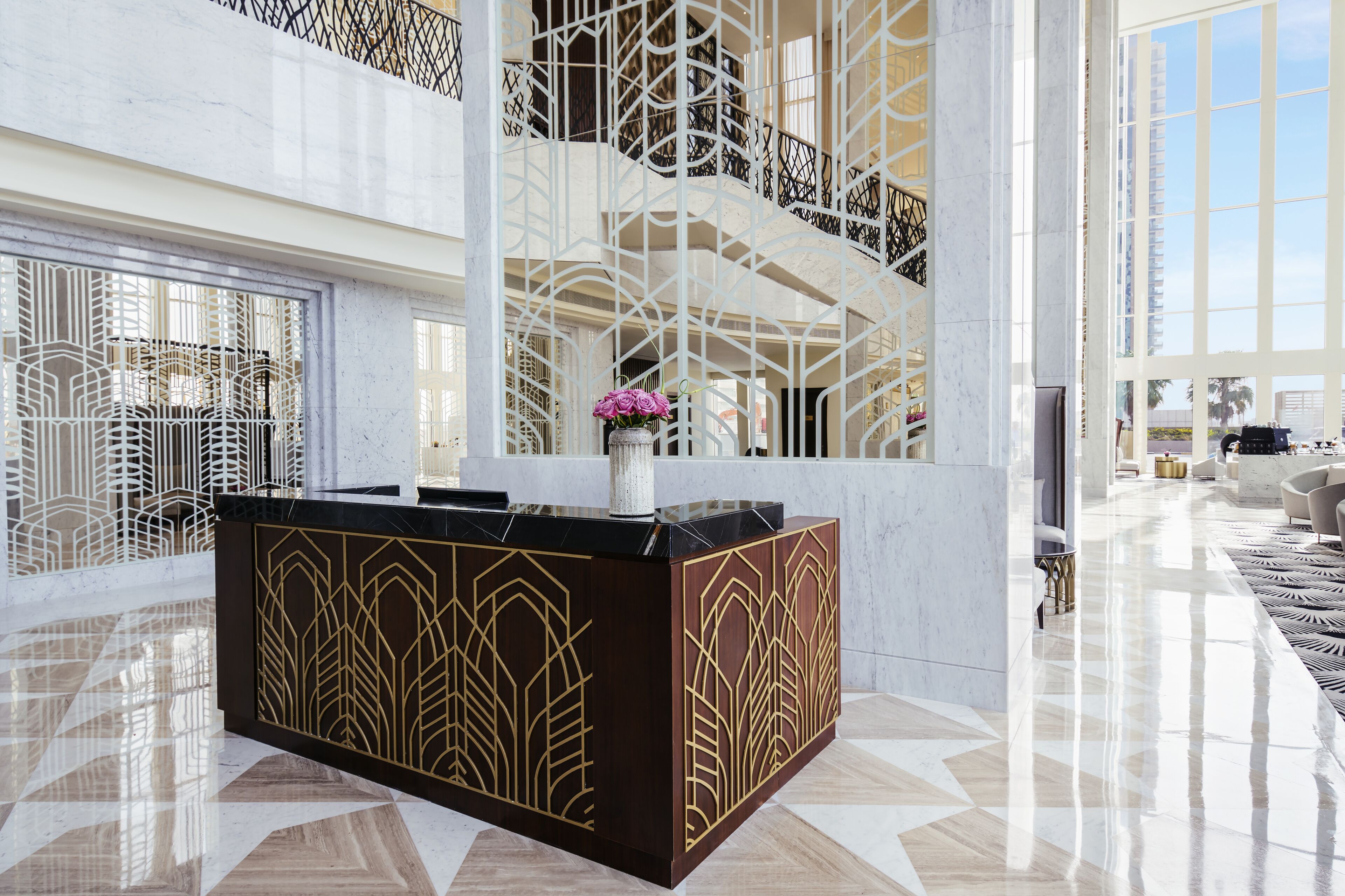 A modern lobby with a marble reception desk, a geometric patterned wall, and a view of the upper floors.