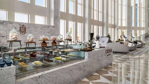Un vaste atrium doté d’un comptoir d’accueil en marbre, d’une vitrine en verre où sont exposées des pâtisseries, et d’un espace détente avec des canapés.