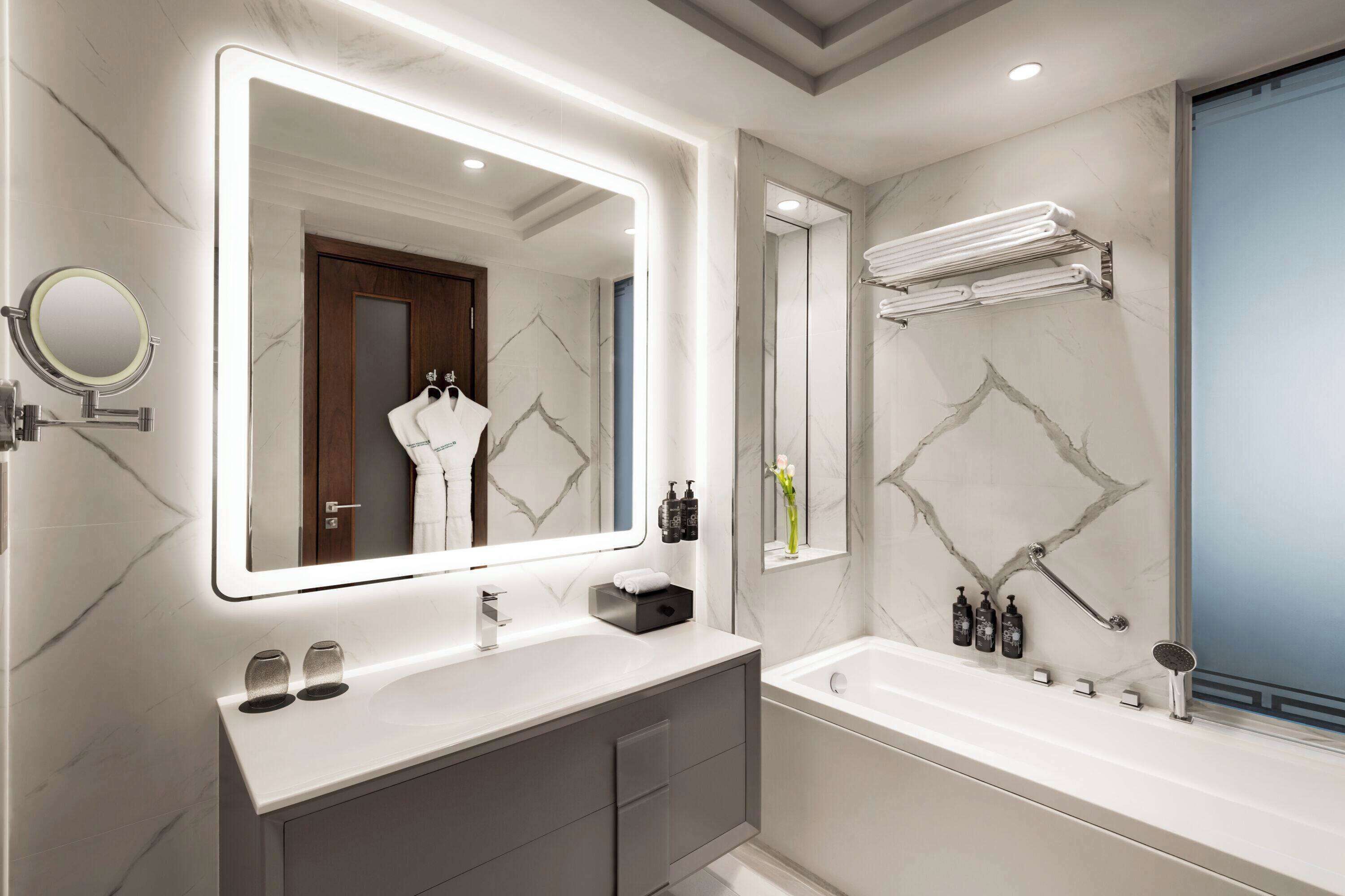 A modern bathroom with a large mirror, a bathtub, and a vanity with a sink.