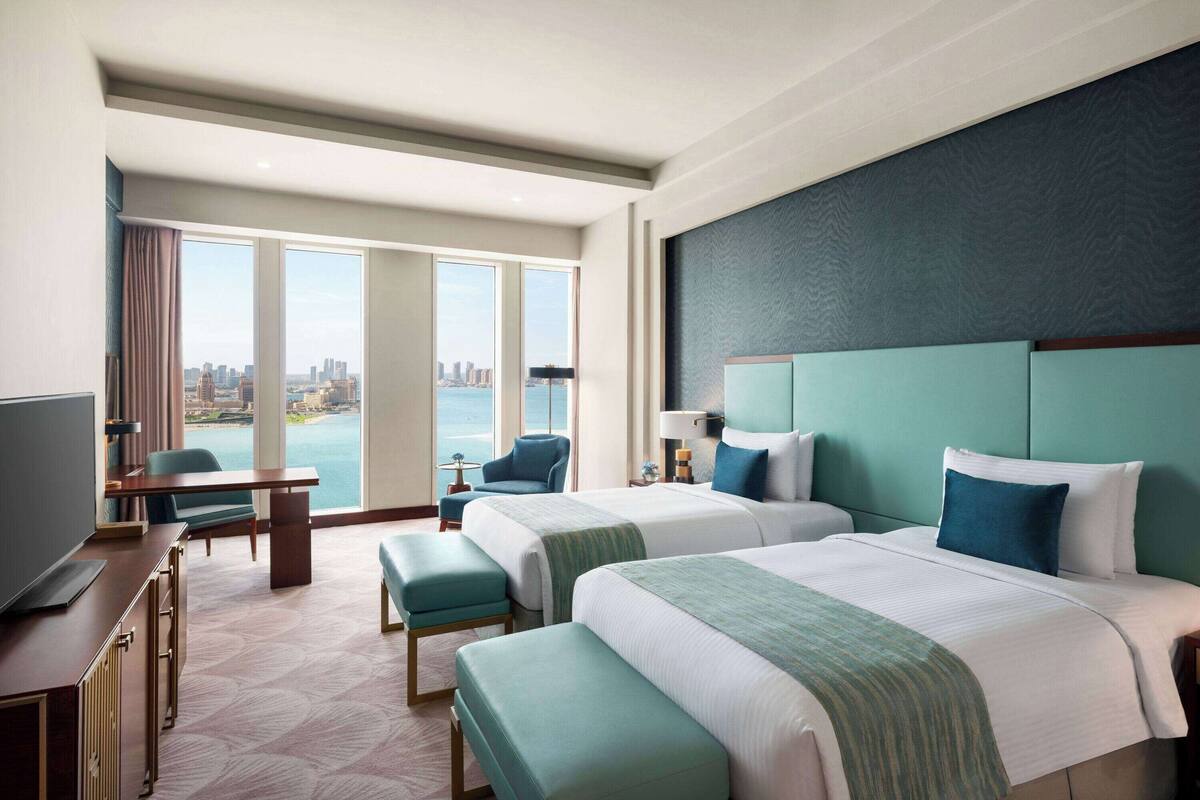 Ein Hotelzimmer mit zwei Betten, einem Schreibtisch, einem Stuhl und einem Fernseher.
