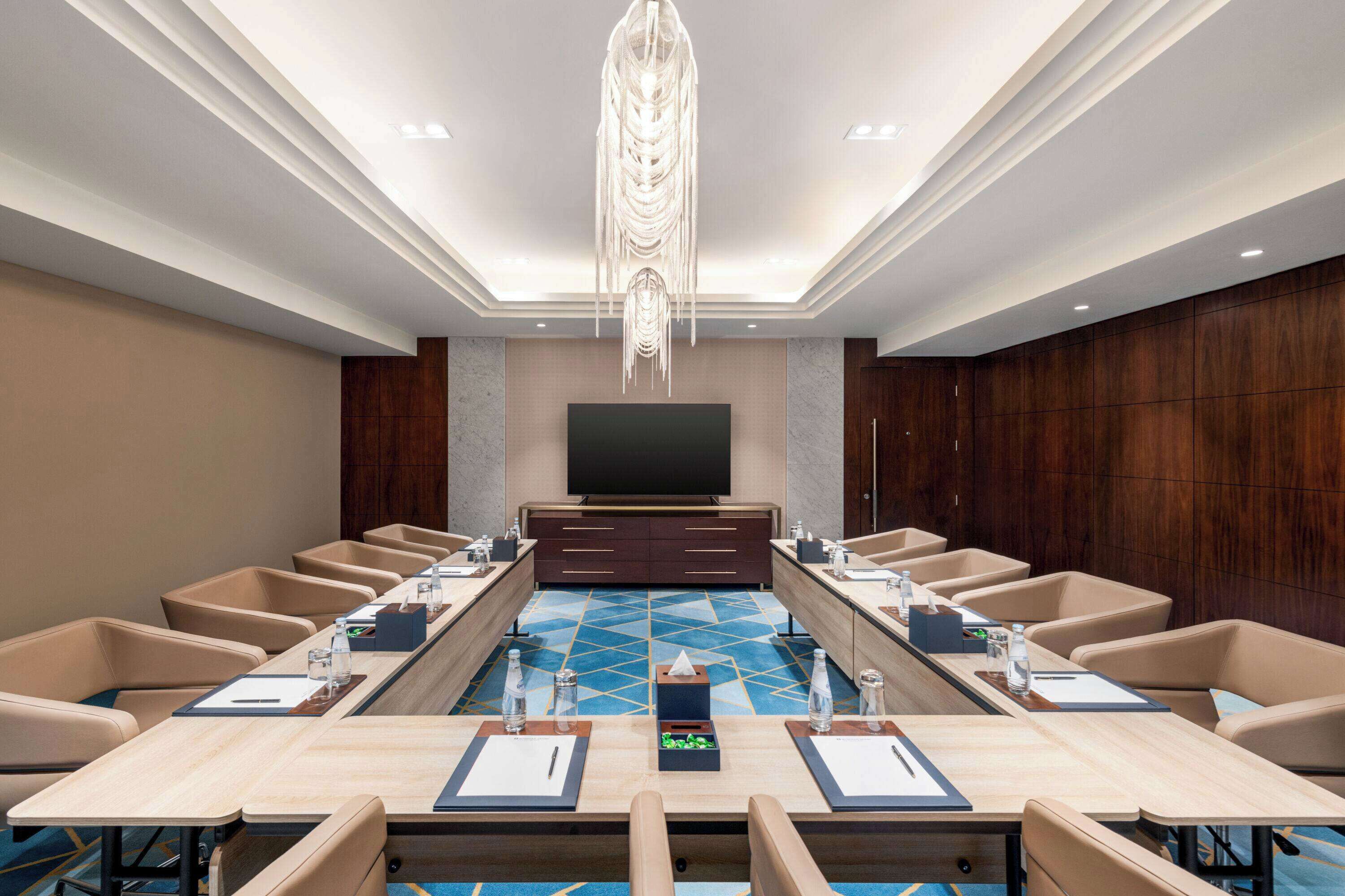 A conference room with a long table, multiple chairs, a television, and a decorative ceiling light.