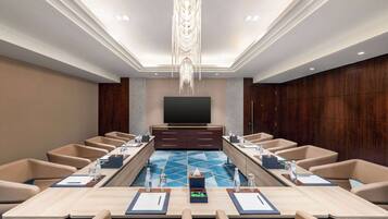 A conference room with a long table, multiple chairs, a television, and a decorative ceiling light.