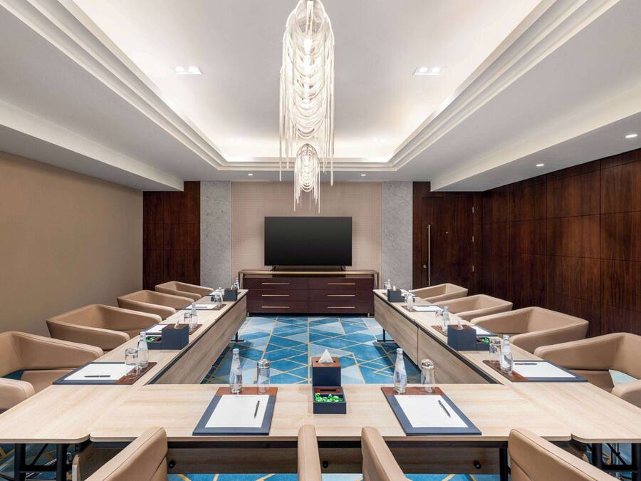A conference room with a long table, multiple chairs, a television, and a decorative ceiling light.