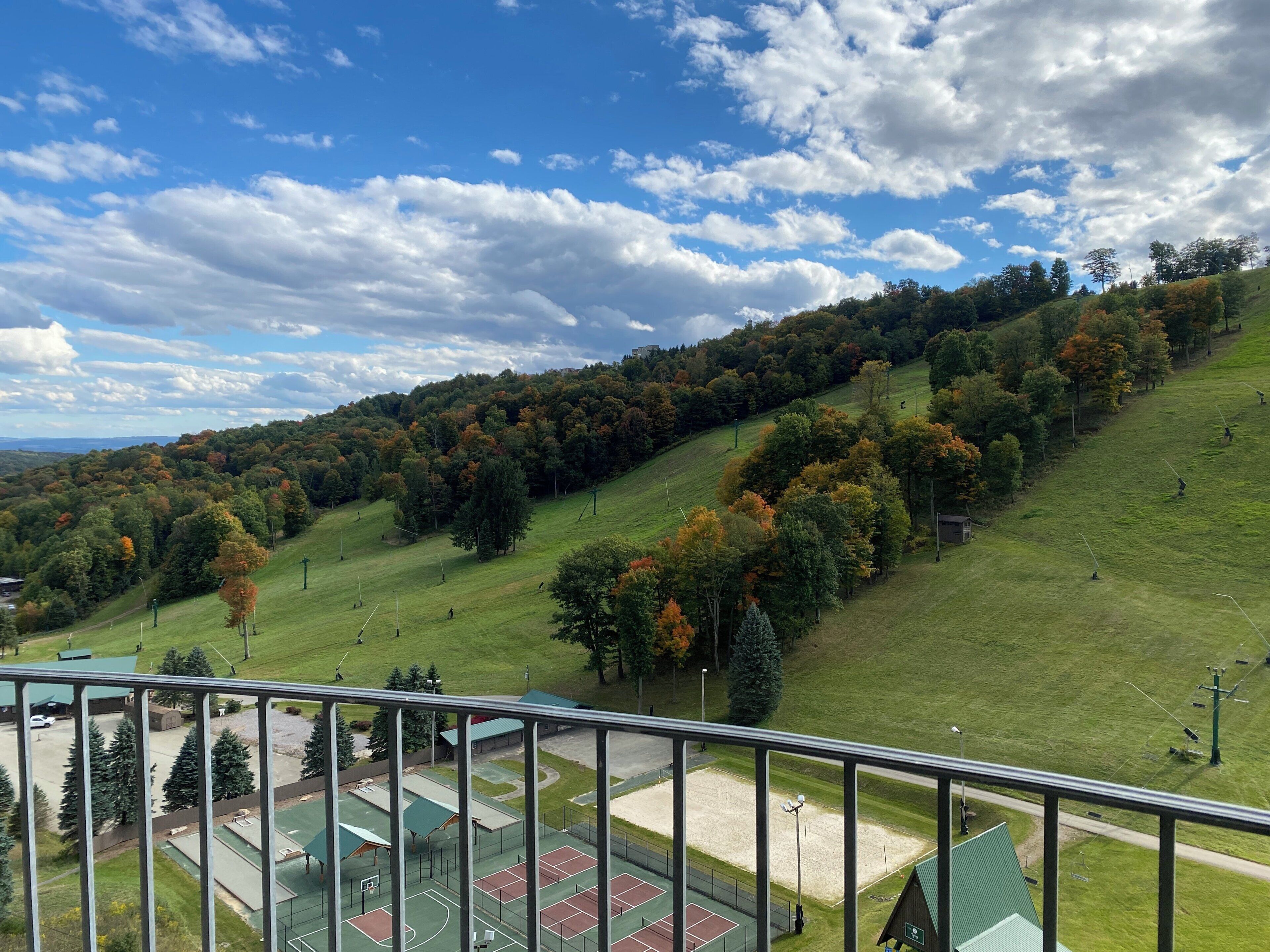 A view from a balcony overlooking a green hillside with trees and a sports court area.