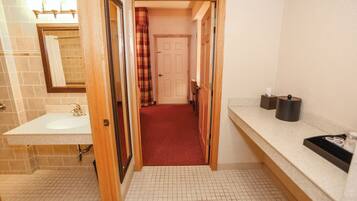 A bathroom with a sink, mirror, and a red carpeted hallway leading to a door.