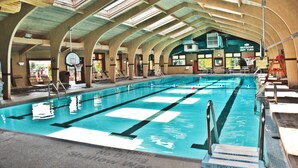 Une piscine intérieure avec des lignes de démarcation bien visibles, un plongeoir et un panneau indiquant l’emplacement des « bains à remous extérieurs ».