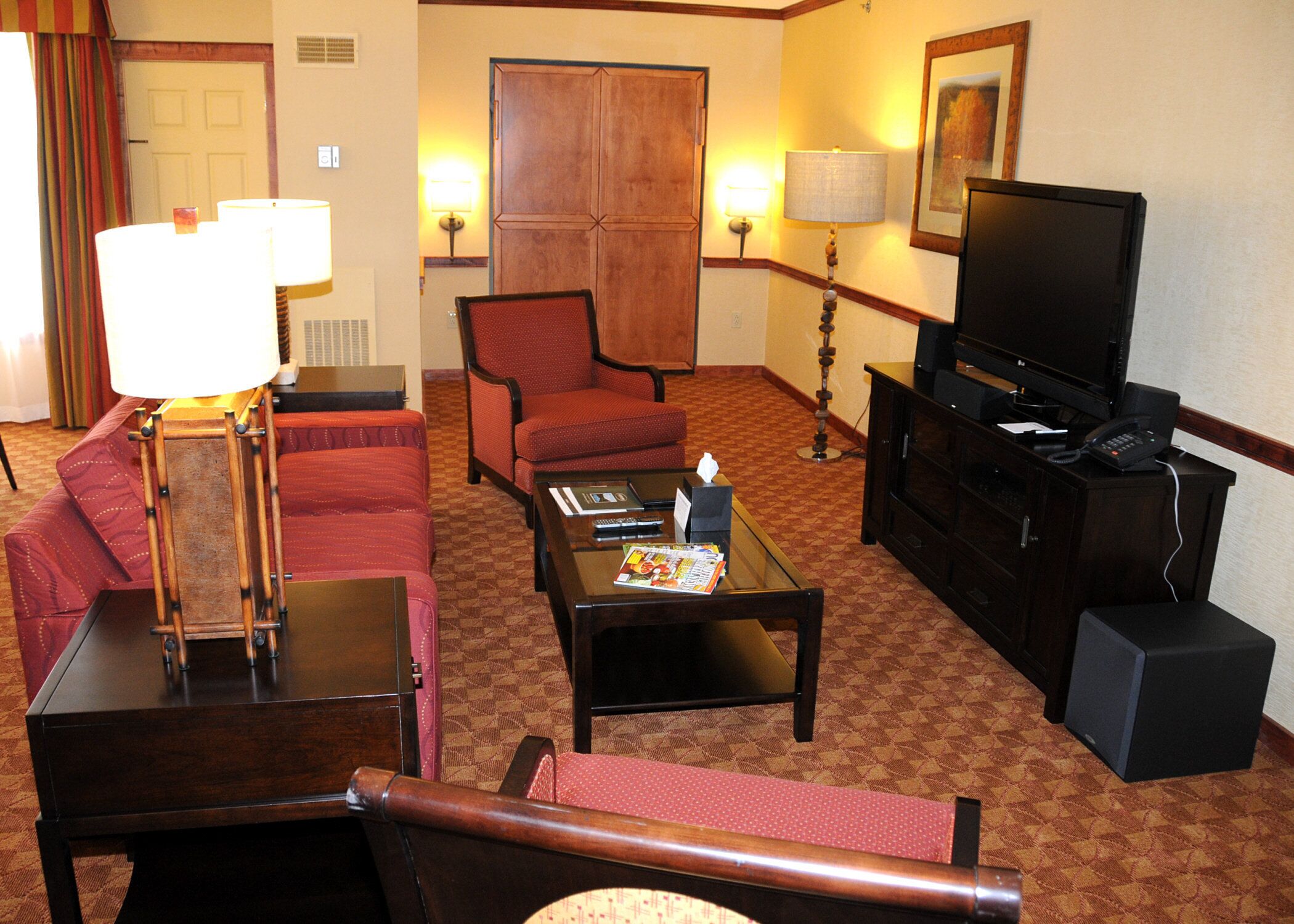 A hotel room with a red sofa, a wooden coffee table, a television, and a lamp.