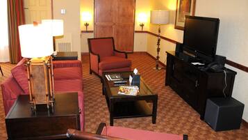 A hotel room with a red sofa, a wooden coffee table, a television, and a lamp.