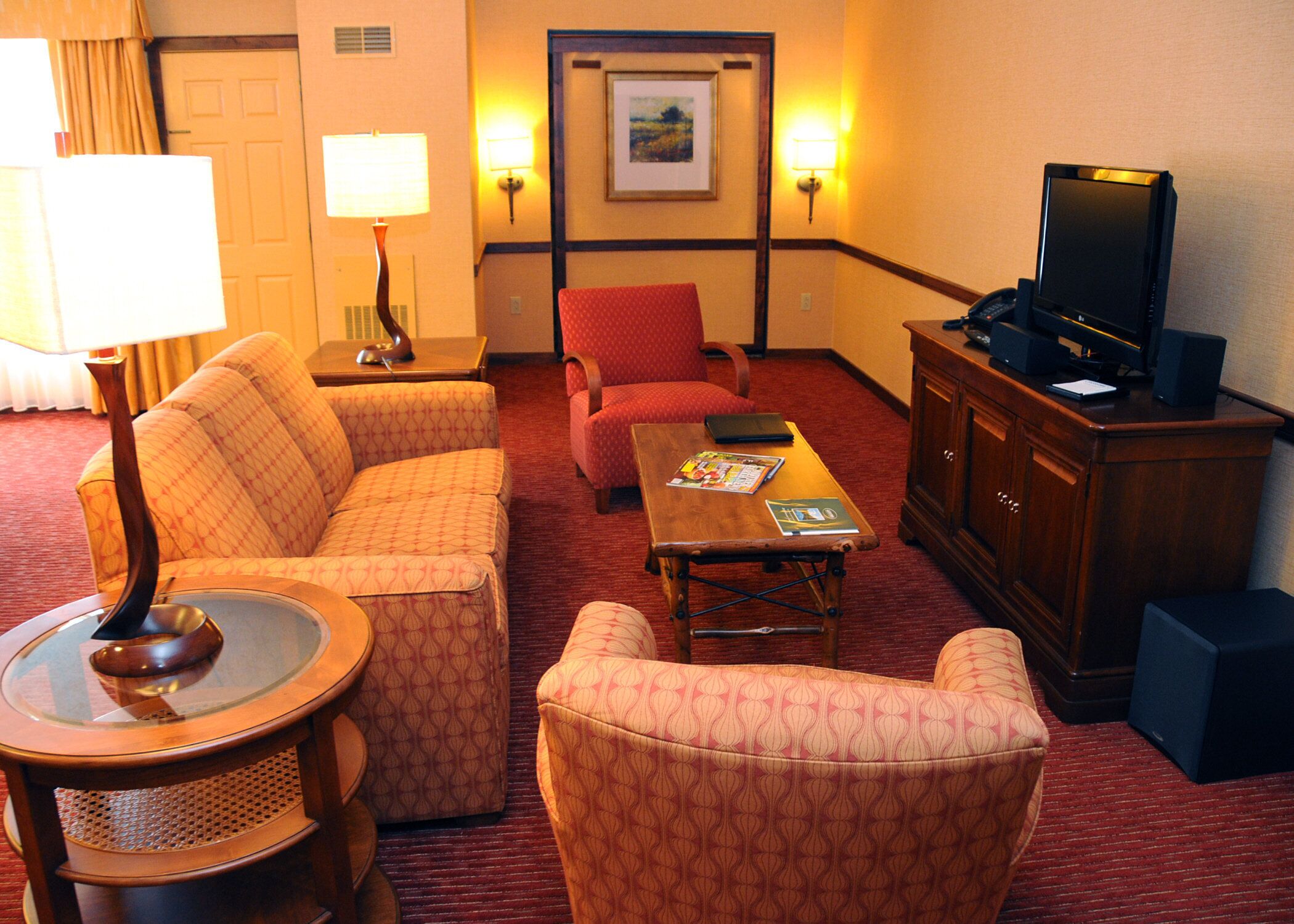 Habitación de hotel con sofá, sillón, mesa de centro, televisor y lámpara.
