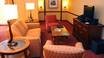 Habitación de hotel con sofá, sillón, mesa de centro, televisor y lámpara.