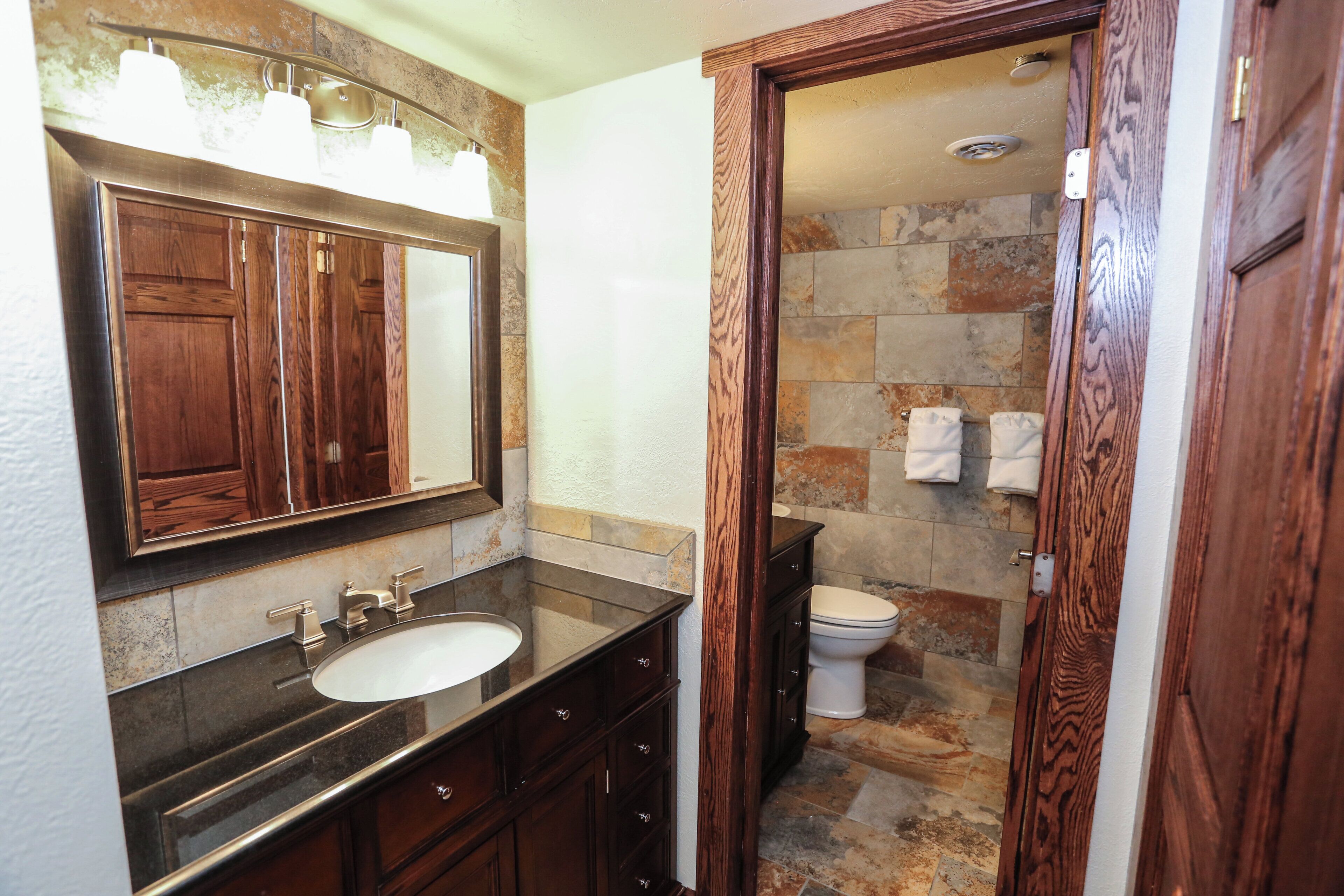 A bathroom with a wooden vanity, a large mirror, a sink, and a toilet.