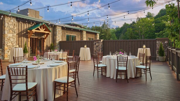 Une terrasse extérieure avec des tables et des chaises rondes, des guirlandes lumineuses et un bâtiment en pierre en arrière-plan.