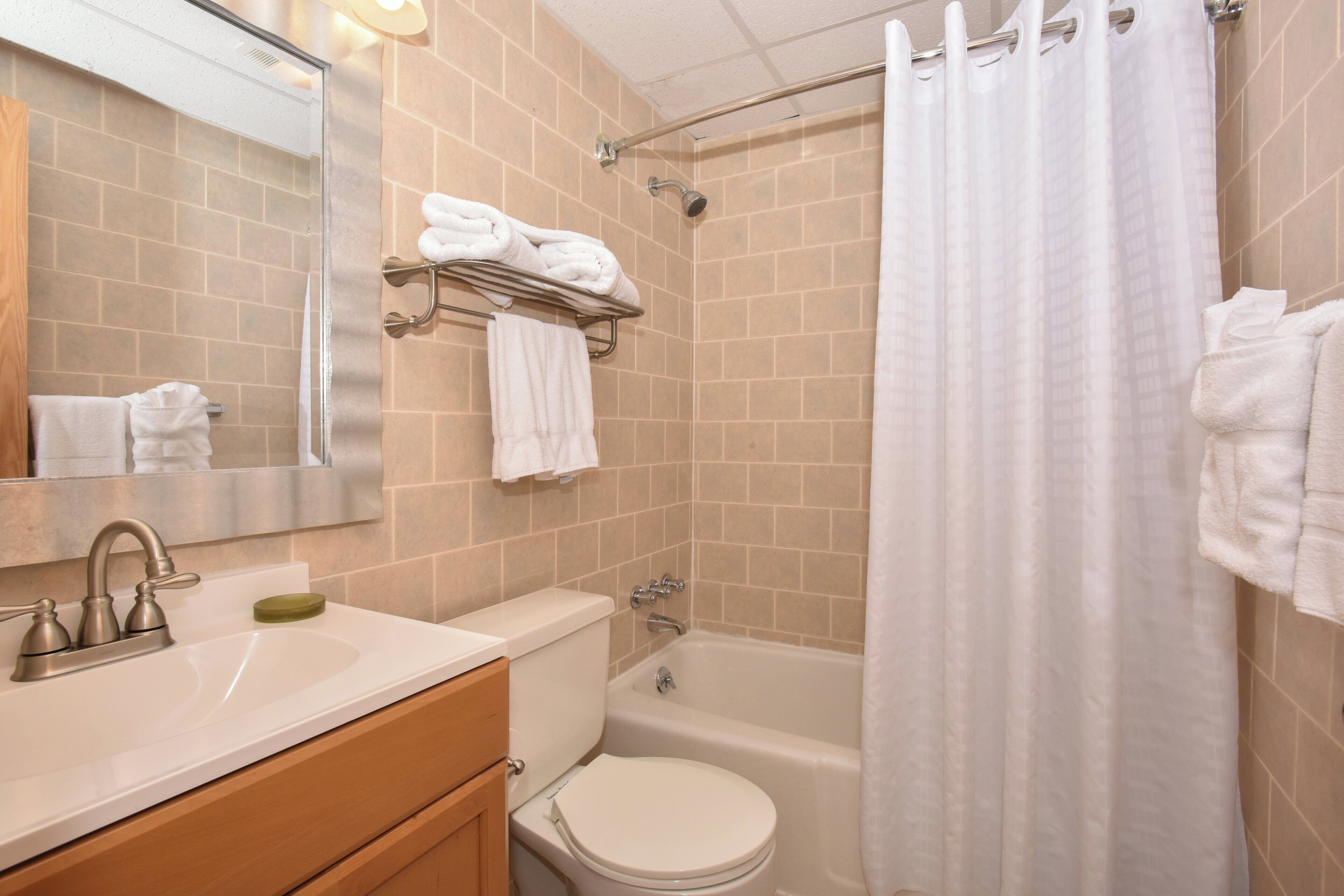 Un baño con lavamanos, inodoro y bañera. Hay toallas en un perchero y una cortina de ducha.