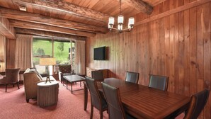 Une pièce aux murs lambrés, comprenant une table à manger, des chaises, un canapé, une lampe et un téléviseur fixé au mur.