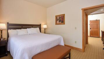 A hotel room with a large bed, two bedside lamps, a wooden bench, a framed picture on the wall, and a wooden door.